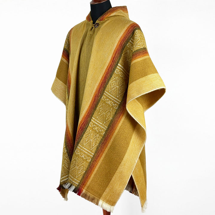 A yellow-brown poncho with colorful stripes and geometric patterns is displayed on a black mannequin against a white background. It has fringe at the edges and a high collar.