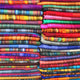 Wholesale lot of 15 queen alpaca wool blankets – colorful fabrics are neatly stacked, displaying vibrant stripes in various hues. They are folded in a layered, orderly arrangement, emphasizing their diverse patterns and textures in a retail setting