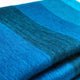 Cajabamba alpaca wool blanket – a folded, fluffy fabric showcasing vibrant blue and teal hues, layered closely, suggesting warmth and softness in an indoor setting