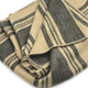 Chalua baby alpaca wool blanket – a folded, beige and dark gray striped blanket lies on a plain white surface, with its soft texture and precise stitching visible