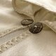 Two large brown buttons sewn onto cream-colored, fringed fabric, possibly a sweater or blanket, lying flat. The image focuses on texture and detail in a softly lit setting.