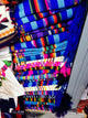 Colorful woven textiles are neatly stacked, displaying vibrant stripes and geometric patterns. The textiles are arranged on shelves, suggesting a market setting with various patterns and textures.