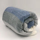 Poguios baby alpaca wool blanket – a rolled-up, striped blanket with shades of blue, gray, and white rests on a plain, light background