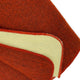 A close-up of an orange fabric with a folded corner, exposing an off-white underside and stitched edges. The texture is visible, emphasizing the material's weave, on a plain background.