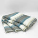 Chuquipogyo baby alpaca wool blanket – a folded blanket featuring horizontal stripes in shades of blue, gray, and white lies stacked against a plain white background, highlighting its soft texture