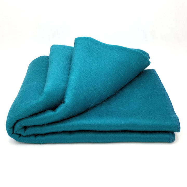 Moyaschucho baby alpaca wool blanket – a folded teal blanket lies neatly on a plain white background, displaying its soft and smooth texture