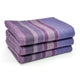 Chuquipata baby alpaca wool blanket – three neatly folded blankets with horizontal purple and lavender stripes are stacked on a white surface, showcasing their soft texture and vibrant colors