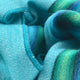 Machay baby alpaca wool blanket – blue and green striped fabric, tightly folded, displaying soft textures and stitched seams, creating a vibrant and cozy appearance
