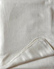 Pilahuin baby alpaca wool blanket – a plain white fabric, shown with a folded corner, rests on a flat surface, displaying its texture and stitch details