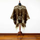 Clint Eastwood alpaca wool poncho – a brown poncho with white geometric patterns is draped over a mannequin. It stands on a wooden floor against a white wall, enhancing its design
