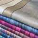Wholesale lot of 15 queen alpaca wool blankets – colorful wool blankets are neatly folded, displaying horizontal stripes in various shades including beige, blue, pink, and multicolored patterns, creating a vibrant stack in a cozy, tactile setting