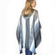 A person wears a hooded poncho with gray and white geometric patterns, standing against a plain white background.