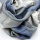 Poguios baby alpaca wool blanket – a soft, multicolored fabric with blue, gray, and white tones lies in gentle folds on a smooth, light-colored surface