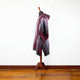 A purple and blue woven shawl drapes over a mannequin stand situated on a wooden floor against a plain white wall.