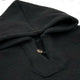 A black hooded garment is laid flat, featuring a single visible button at the neckline, surrounded by a plain white background.