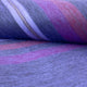 Punguloma baby alpaca wool blanket – a roll of textured fabric with purple, pink, and red stripes lies partially unrolled on a flat surface, showcasing its soft, wool-like material and vibrant pattern