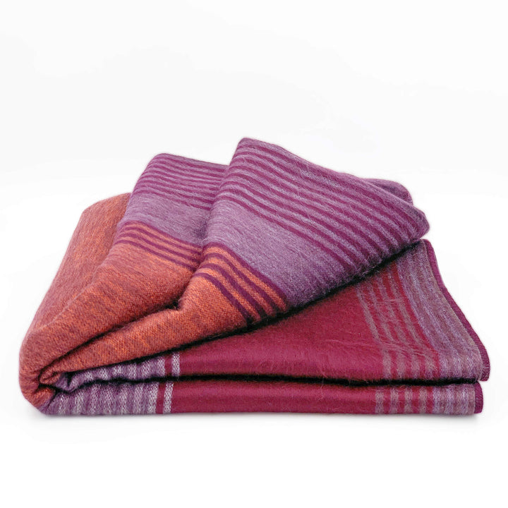 Pallatanga baby alpaca wool blanket – a folded wool blanket displays alternating purple and orange stripes, resting on a white background, highlighting its soft and textured appearance