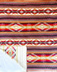 Rug displays intricate geometric patterns in red, orange, and white, featuring diamonds and lines. Corner folded over reveals beige underside with lighter geometric design, showcasing textile's thickness.