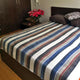Siguitag alpaca wool throw blanket – a striped blanket covers a neatly made bed with two pillows, next to a wooden bedside table holding a vase of red roses in a cozy bedroom setting