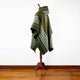 A green and white striped poncho with a hood drapes over a wooden mannequin stand in a room with wooden floors and a white wall.