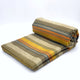 Rumi baby alpaca wool blanket – a neatly folded blanket features horizontal stripes in earthy tones, including orange, yellow, and grey, resting on a white surface