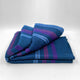 Tamboloma baby alpaca wool blanket – a folded blue blanket with pink and purple stripes lies on a flat, white surface