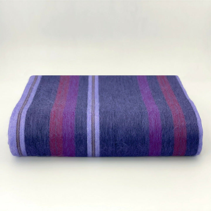 Punguloma baby alpaca wool blanket – a folded blanket rests on a flat surface, featuring horizontal stripes in shades of purple, red, and blue, set against a plain, light-colored background