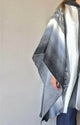 A person wearing a gray and white patterned poncho stands against a plain backdrop, with only their arm and torso visible. The poncho drapes elegantly over blue jeans.