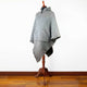 A gray hooded poncho with a front pocket is displayed on a wooden stand against a plain white background on a hardwood floor.