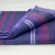 Punguloma baby alpaca wool blanket – a folded blanket featuring purple, pink, and grey stripes lies on a smooth, light-colored surface. The blanket's texture appears soft and slightly fuzzy