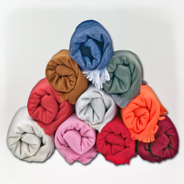 Colorful fabric rolls are stacked in a triangular formation, featuring shades of blue, green, red, orange, pink, and more, against a plain white background.