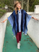 A person wearing a blue poncho and brown hat walks along a green pathway, bordered by white walls, with trees visible in the background.