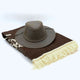 A brown leather hat rests on a neatly folded, fringed wool blanket, set against a plain white background.