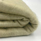 Llullalo baby alpaca wool blanket – a folded, beige woolen blanket lies on a flat, white surface, showcasing its soft, textured fibers in a simple, clean setting