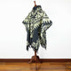 Tarqui alpaca wool hooded poncho – a patterned poncho drapes over a wooden mannequin stand, featuring geometric designs and fringes. It is set against a plain white wall and wooden floor