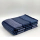 Chimborazo baby alpaca wool blanket – a folded blue and gray striped blanket lies flat, with varied hues creating a pattern, situated against a plain white background
