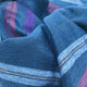 Tamboloma baby alpaca wool blanket – a blue woolen blanket features red and purple stripes, arranged in soft folds, suggesting comfort and warmth in a cozy setting