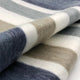 Pilishurco baby alpaca wool blanket – a soft woolen fabric draped in thick horizontal stripes featuring blue, gray, and beige tones, lying on a smooth surface