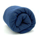 A blue wool blanket is rolled tightly in a cylindrical shape, resting on a white surface with no visible patterns or additional objects in the surroundings.