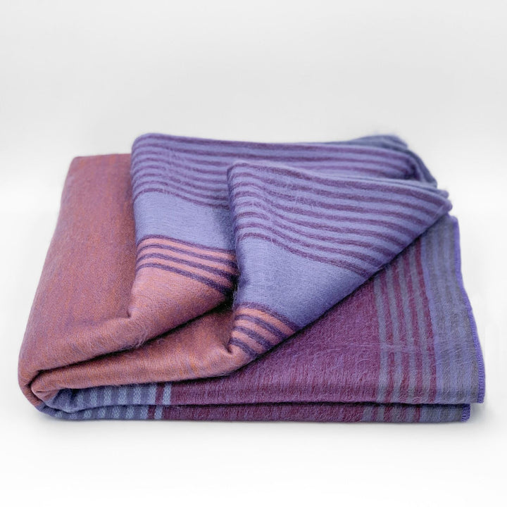 Ochoa baby alpaca wool blanket – a folded, striped, purple and pink blanket rests on a white background, showcasing its soft texture and alternating colors