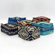 Five fabric face masks with colorful, geometric patterns rest on a white surface. The designs feature combinations of blue, brown, and black, presenting a vibrant display.