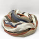 Siguitag alpaca wool throw blanket – a multicolored blanket featuring stripes of white, gray, blue, orange, and brown is loosely coiled on a plain, light background