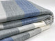 Poguios baby alpaca wool blanket – a folded, striped blanket featuring shades of gray, blue, and white lies neatly stacked on a white surface, suggesting a cozy, organized setting