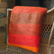 Yacupungu baby alpaca wool blanket – a blanket with red and orange horizontal stripes is draped over a woven rattan chair, situated in a cozy indoor setting with muted lighting
