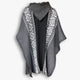 A gray hooded poncho hangs with intricate white geometric patterns on the borders, set against a plain, light background.