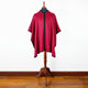 A red wool cape with black trim displayed on a dress form in a room with wooden flooring and white walls.