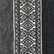 A textile features intricate diamond and geometric patterns in black and white, woven centrally, with solid black textured fabric on either side, creating a striking contrast.