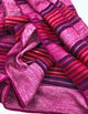 Cayetana baby alpaca wool blanket – pink and purple textured fabric is draped with visible folds, featuring striped patterns of alternating colors. The background is a plain, light surface