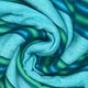 Machay baby alpaca wool blanket – the fabric, with swirling blue and green stripes, displays a spiral pattern, creating an intricate and colorful texture. It appears soft and woven, suggesting warmth and comfort