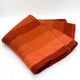 Cusubamba baby alpaca wool blanket – a folded blanket features horizontal stripes in varying shades of orange and red, resting on a plain white background